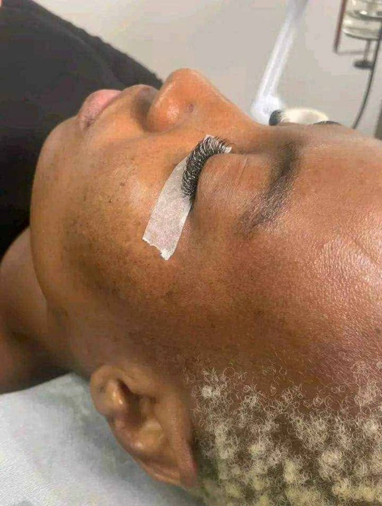 Client lying back during a lash appointment, with protective tape under the eye and lashes applied to the upper lid